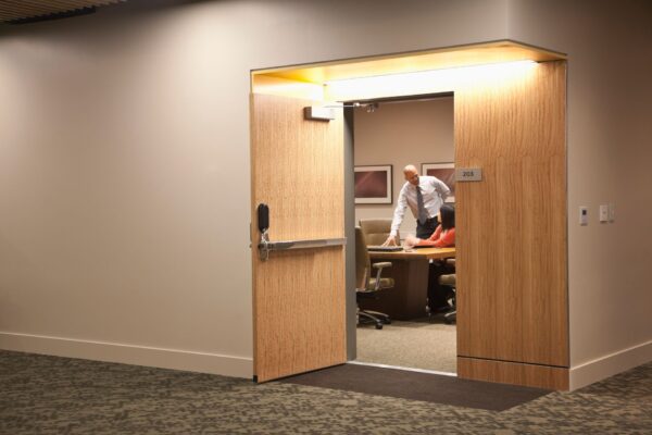 A smart lock on an open office door, two people can be seen in the office.